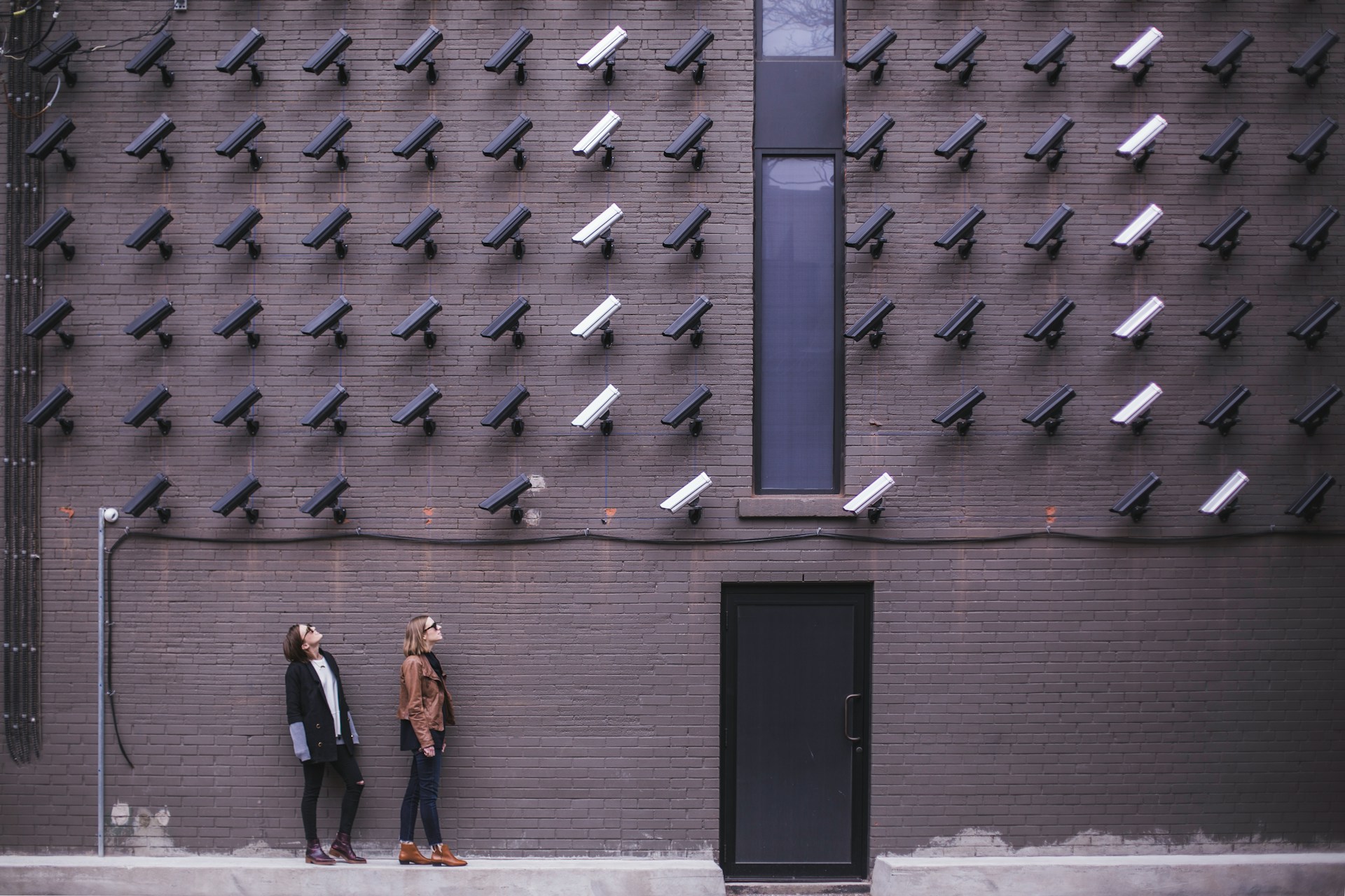 Two people looking up at rows of security cameras mounted on a brick wall